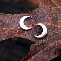 Silver New Moon Post Earrings set against the dark brown of an oak leaf, accentuating their bright silver sheen.