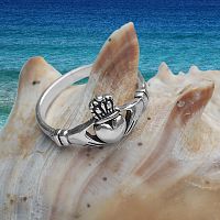 Artistic shot of the Silver Irish Claddagh Ring perched on a seashell, with the distant ocean as a backdrop.