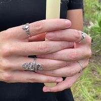 A woman's interlaced fingers holding an upright candle, adorned with various rings including the Silver Irish Claddagh Ring.