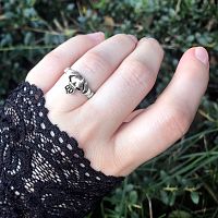 A female hand with a black lace cuff, wearing the Silver Irish Claddagh Ring with the heart facing outward.