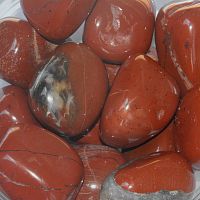 Tumbled Red Jasper gemstones in natural shapes, displaying their rich terracotta red tones and inherent streaks and markings.