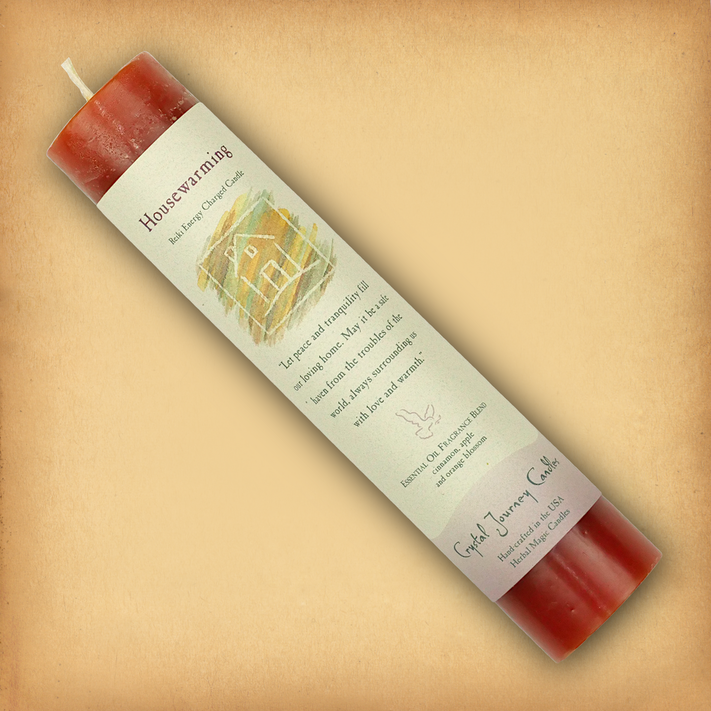 Orange Reiki-charged Housewarming Pillar Candle, laid diagonally to show its label with affirmation and essential oil blend.