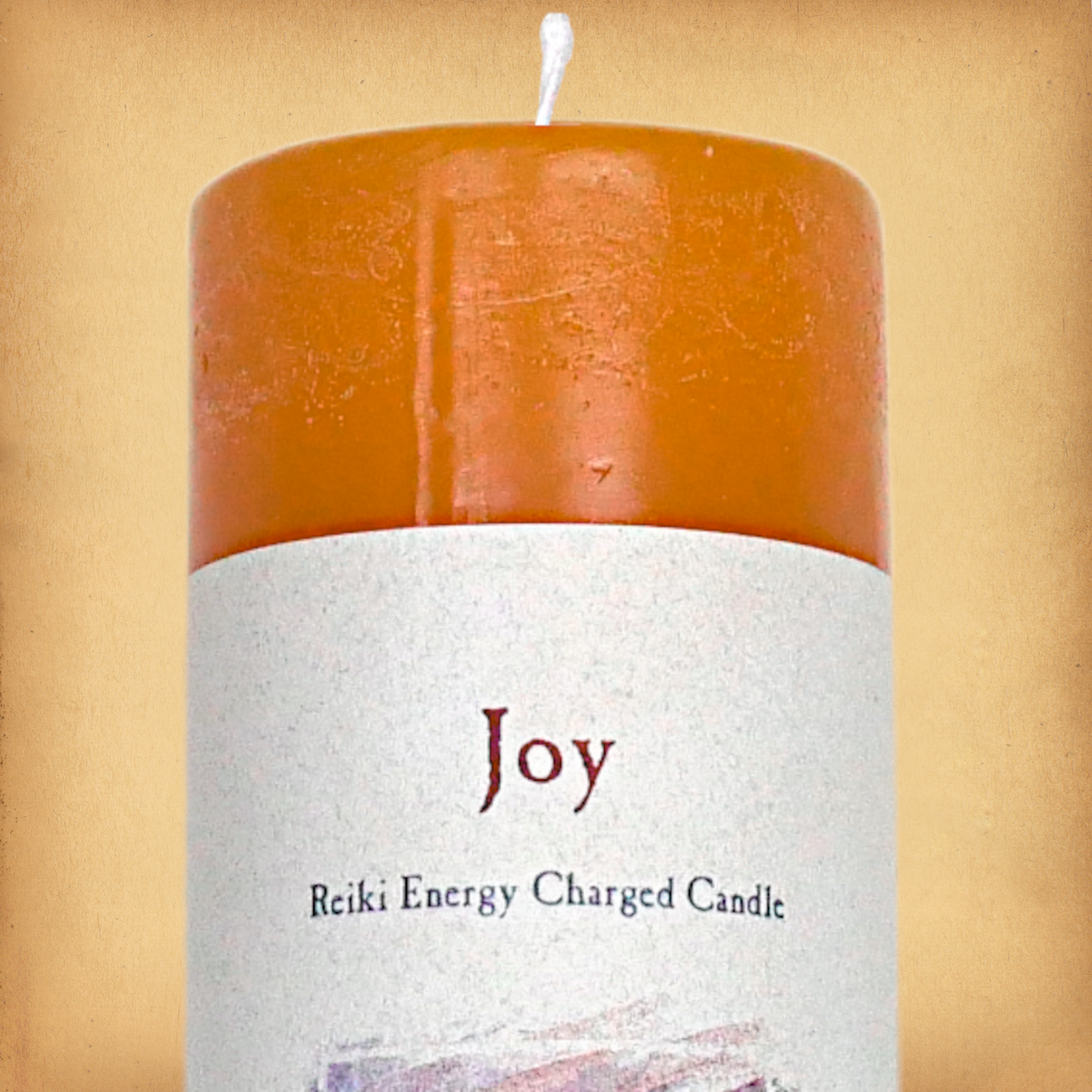 Orange pillar candle labeled “Joy” with “Reiki Energy Charged Candle” beneath. Slim pillar candle with a single wick.