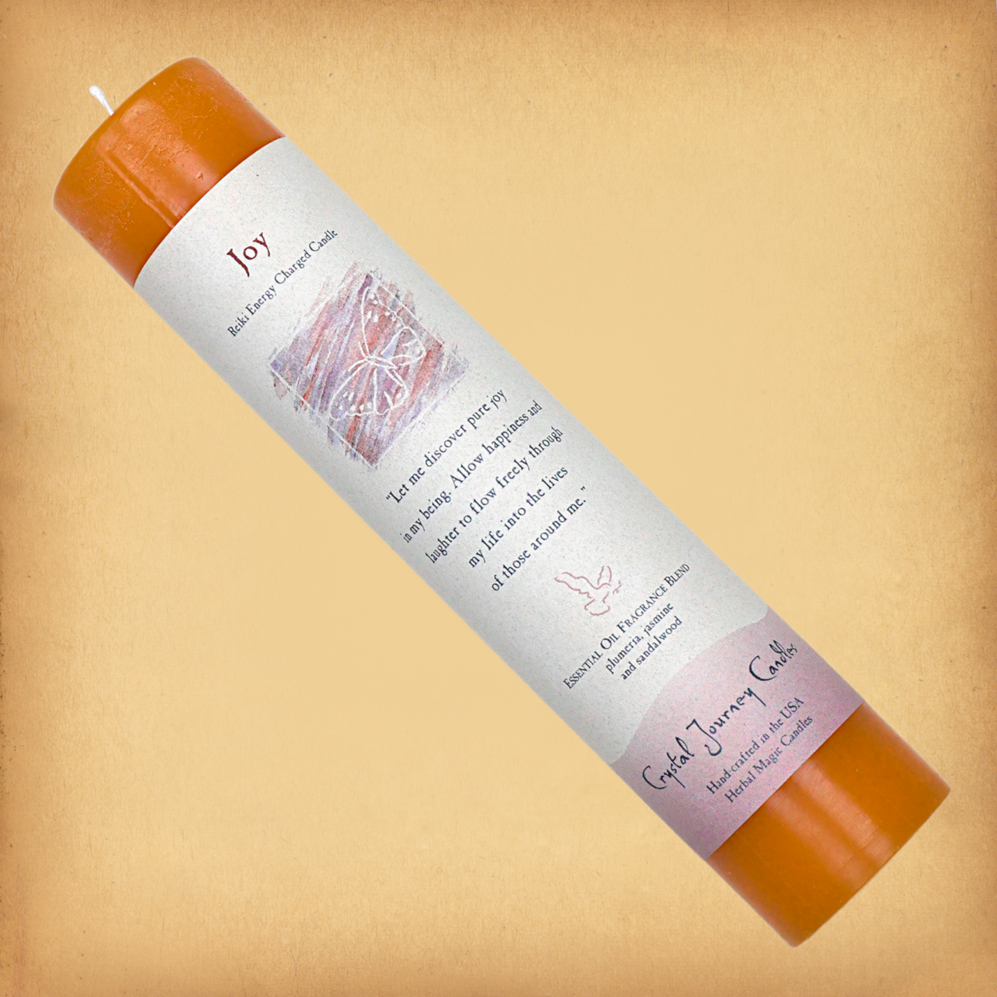 Orange Reiki-charged Joy Pillar Candle, displayed diagonally to show its label with affirmation and essential oil blend.