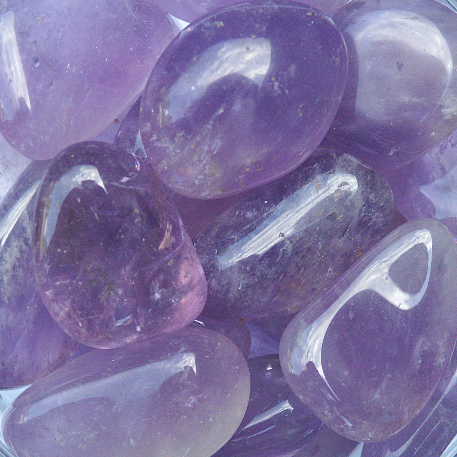 Tumbled Amethyst gemstones in soft to deep purple hues, with polished surfaces and natural inclusions adding minor variations