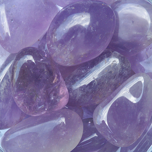 Tumbled Amethyst gemstones in soft to deep purple hues, with polished surfaces and natural inclusions adding minor variations