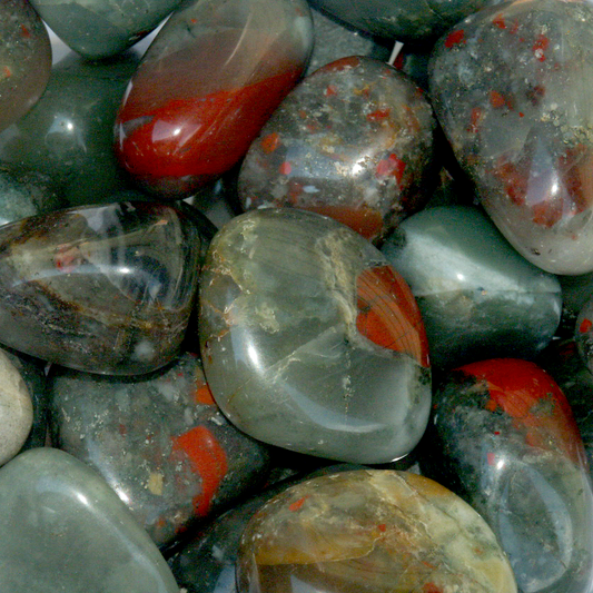 Tumbled Bloodstone gemstones showcasing a spectrum from deep mossy green to smoky gray, accented with scattered flecks of red