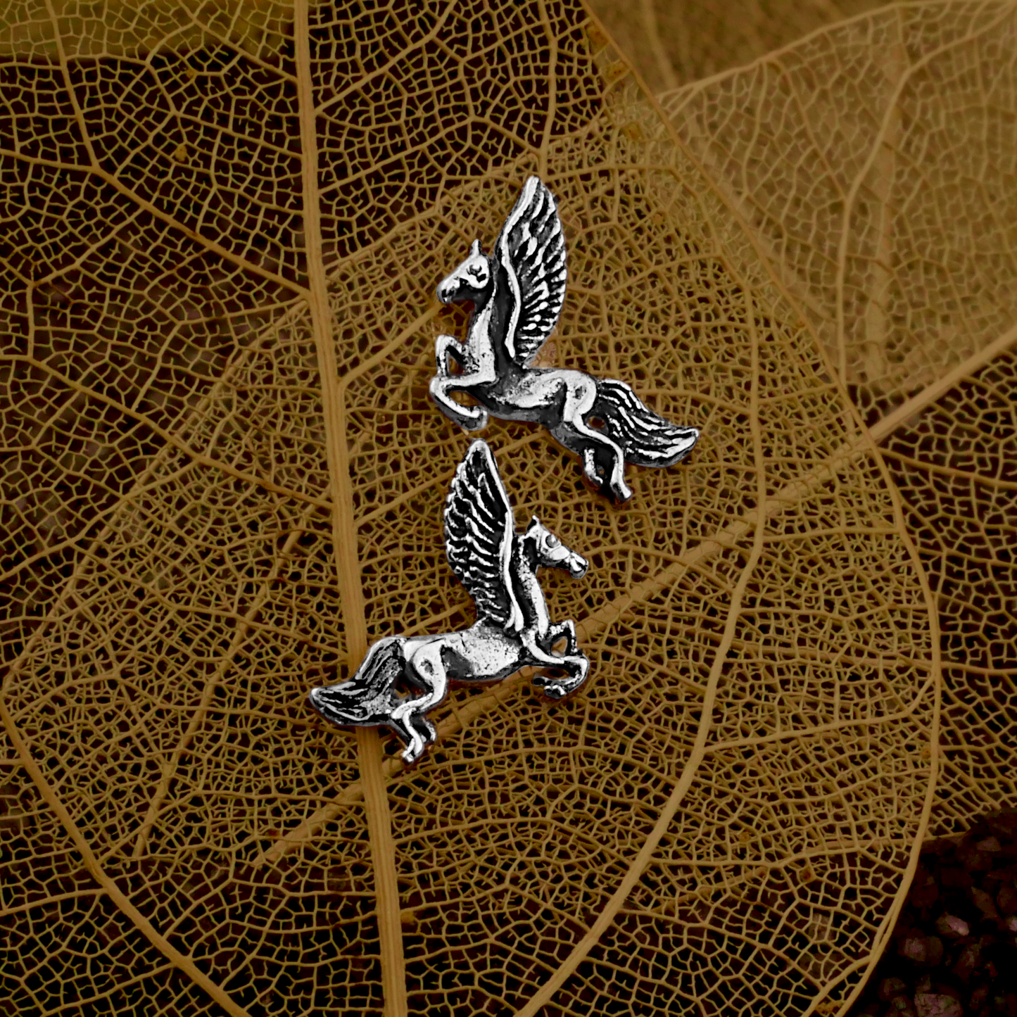 Silver Pegasus Post Earrings on a backdrop of delicate leaf skeletons, accentuating their dainty design.