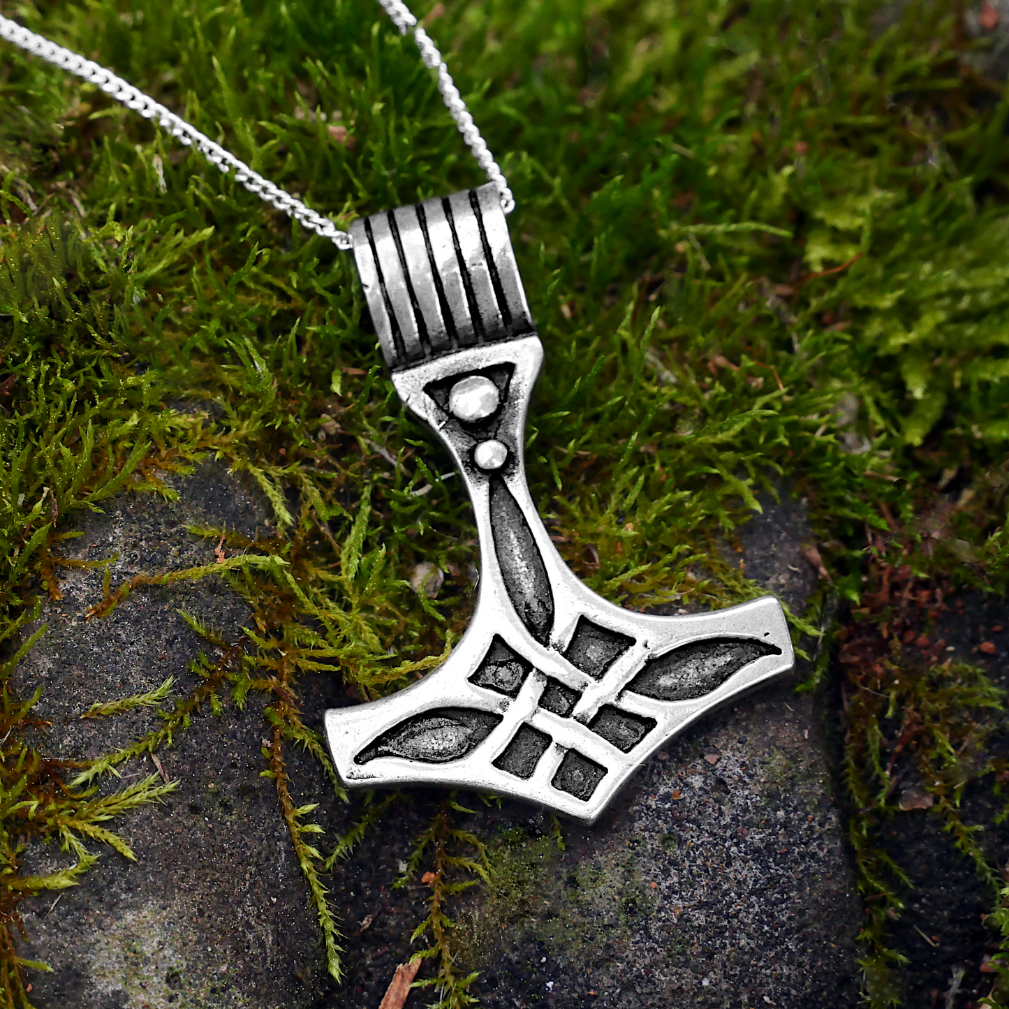 Thor's Hammer Pendant in sterling silver with bold Celtic knotwork and silver chain, displayed on a natural mossy background.
