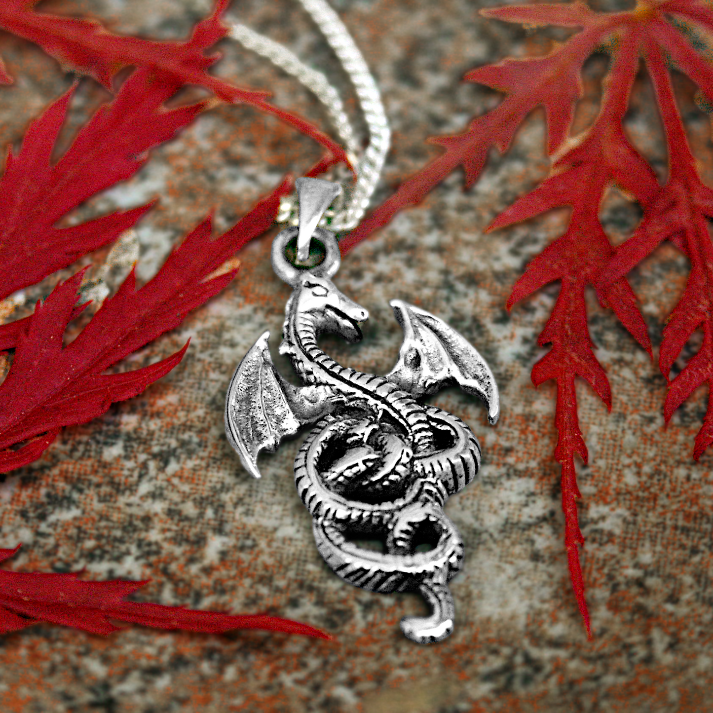Sterling Silver Coiled Dragon Pendant displayed with red maple leaves, showcasing its intricate design and fierce elegance.