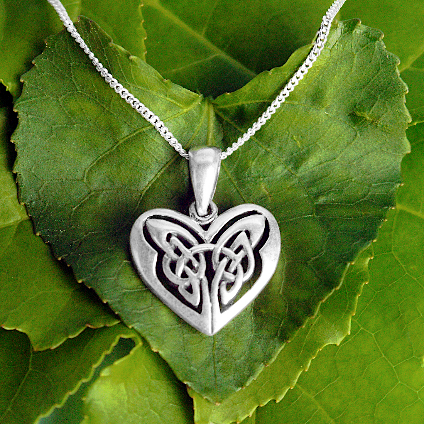 Sterling Silver Celtic Heart Pendant on a delicate silver chain, displayed on a heart-shaped green leaf for a natural touch.