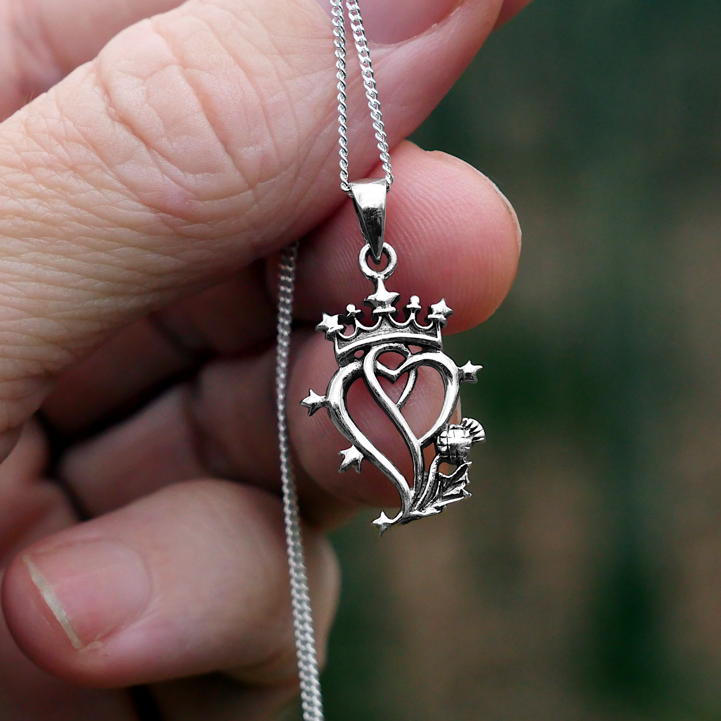 Silver Thistle Luckenbooth Pendant held in a woman's fingertips, showing its relatively small size and delicate appearance.