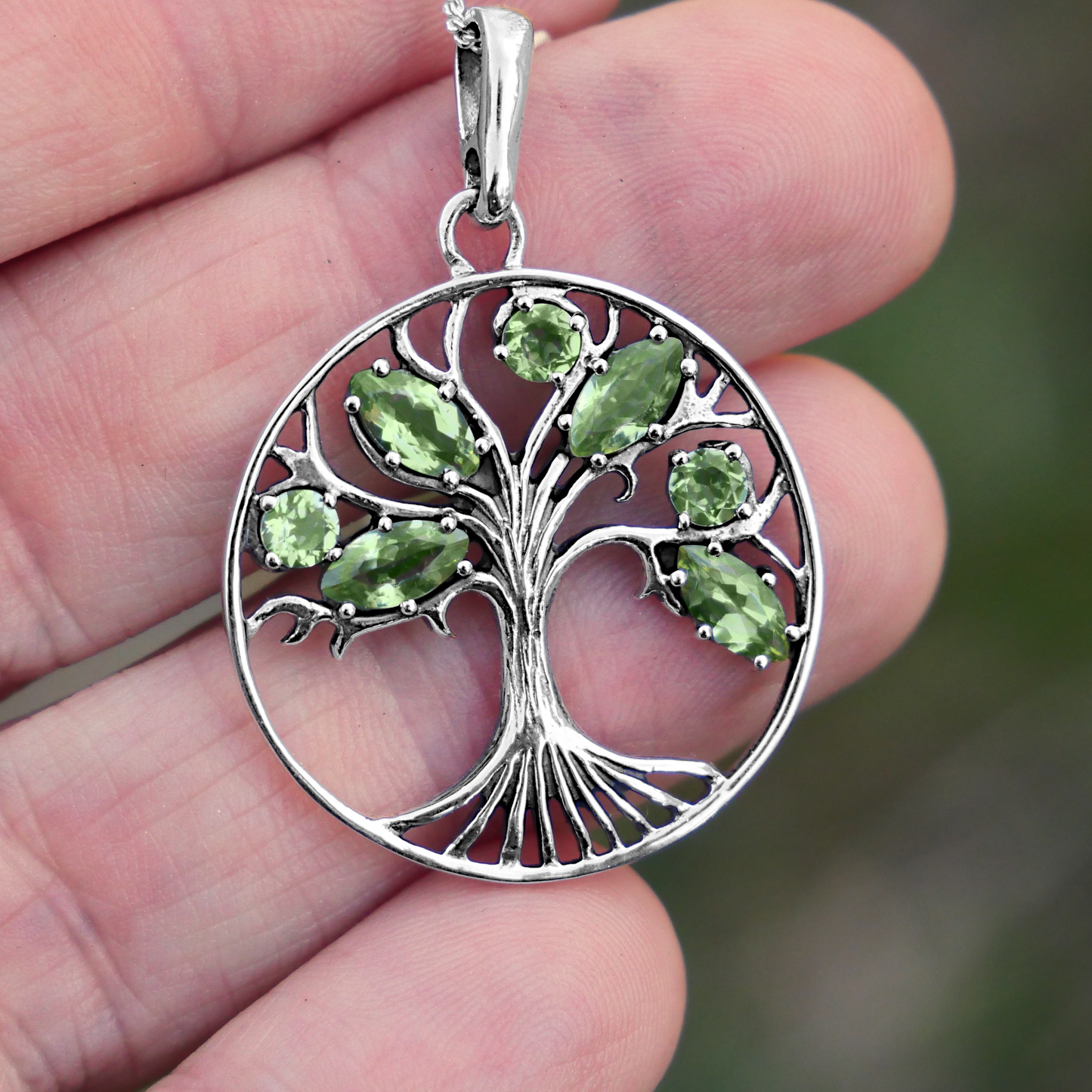 Sterling Silver Peridot Tree Pendant held between fingertips, highlighting the fine details in the tree’s roots and branches.