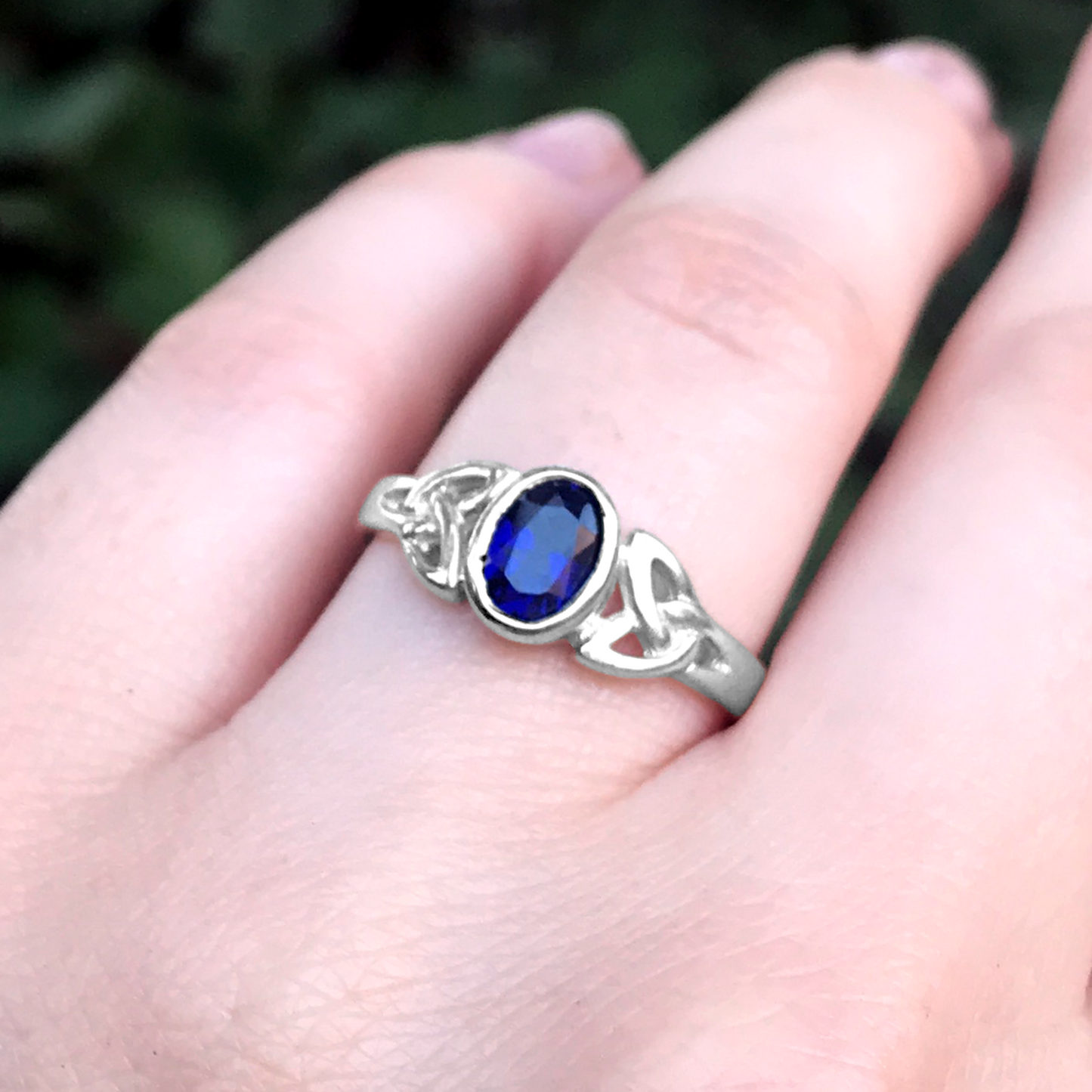 Sterling Silver Sapphire Celtic Ring with a vibrant blue faceted gemstone, captured in a detailed close-up on a graceful hand