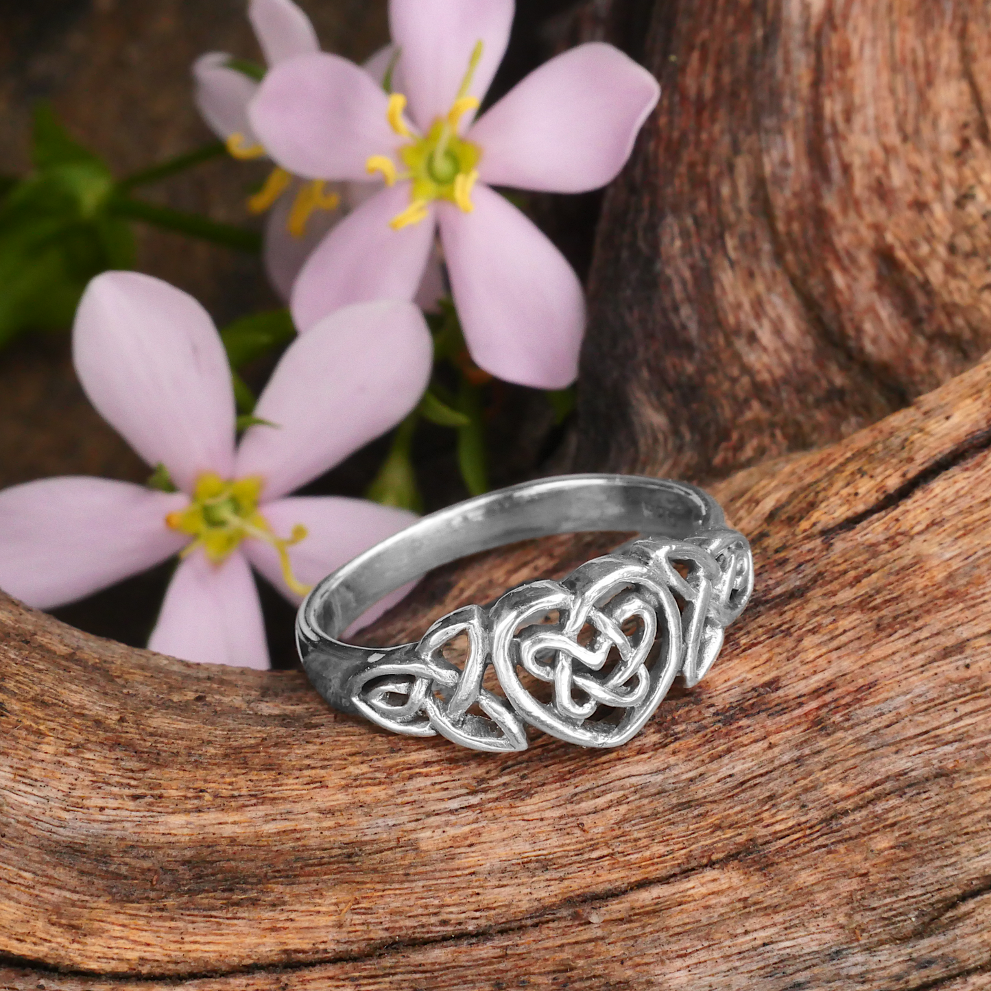 Sterling Silver Celtic Heart Ring, showcasing its Celtic knot design, set against weathered wood and delicate pink flowers.