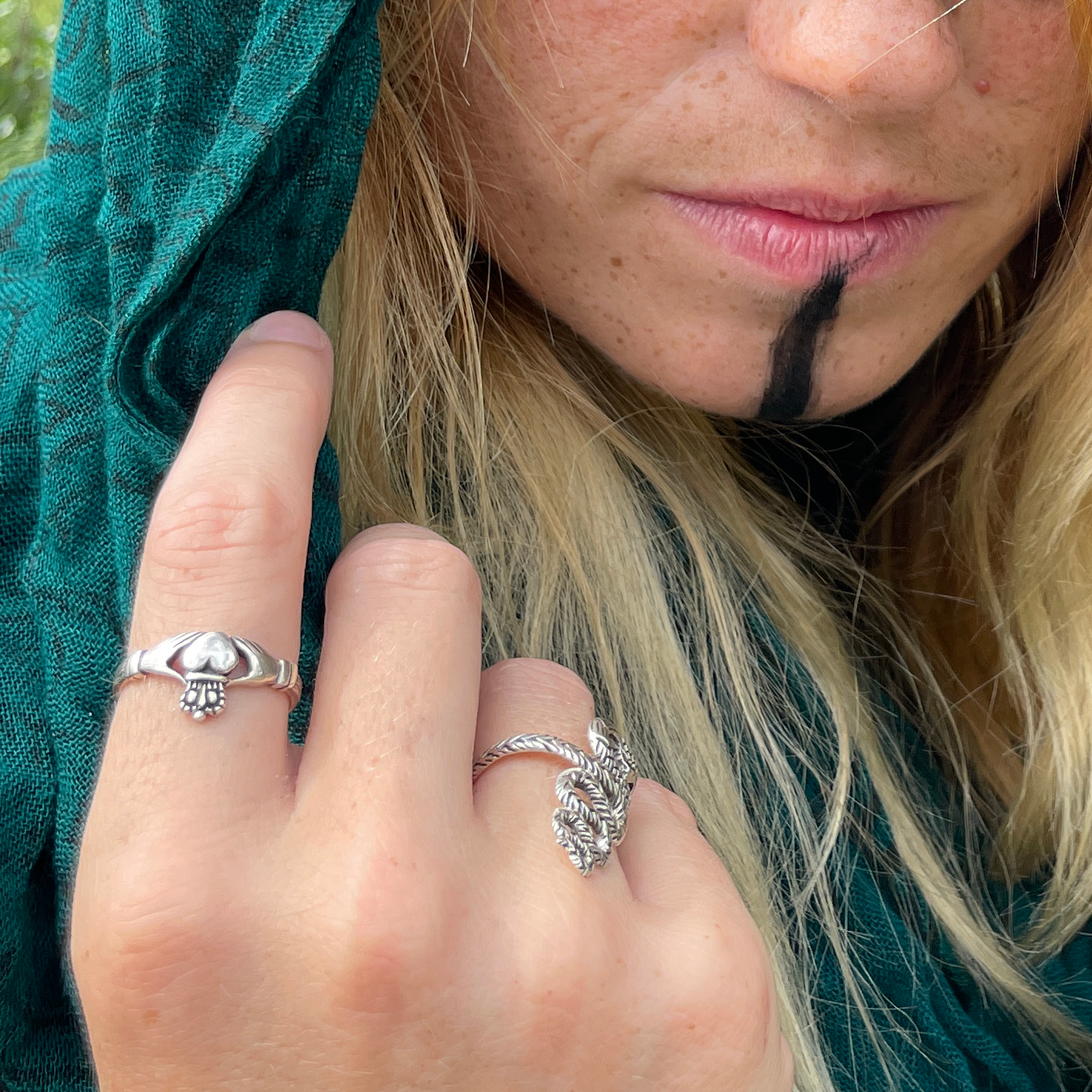 Closeup of a woman's hand adorned with a Silver Irish Claddagh Ring, partially revealing her enigmatic face.