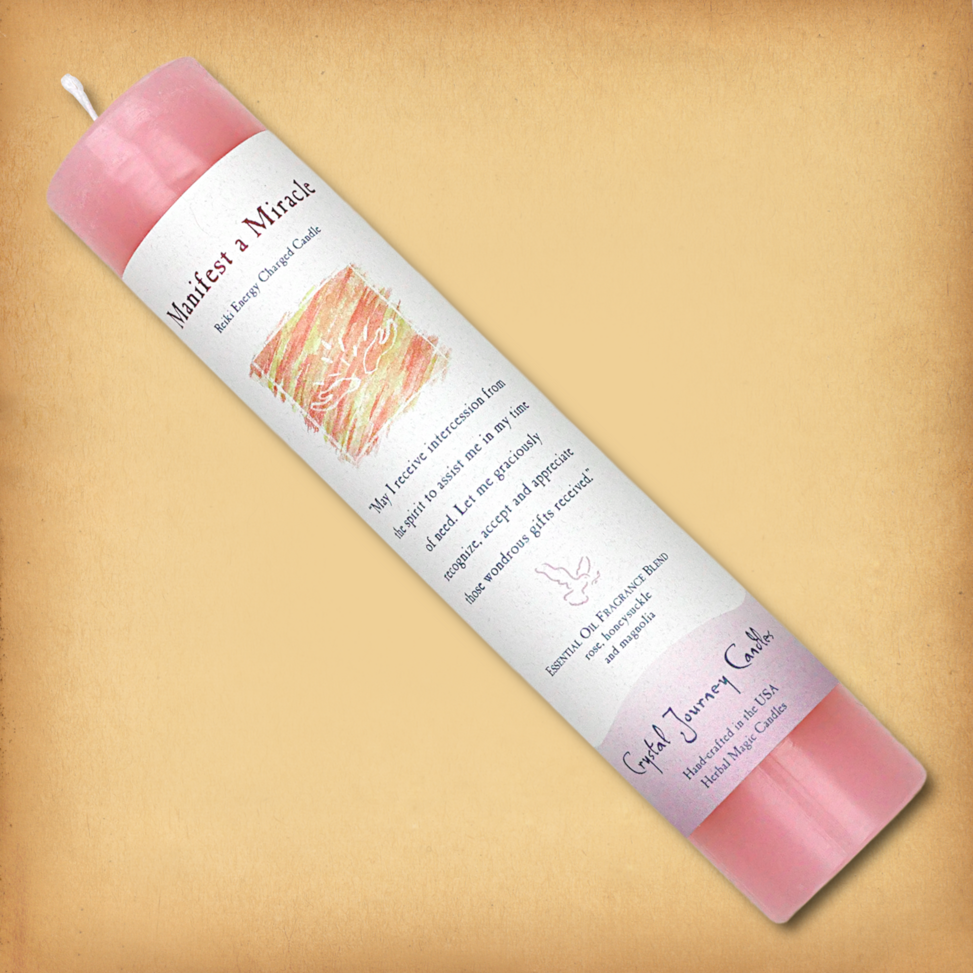 Pink Reiki-charged Manifest a Miracle Pillar Candle, laid diagonally to show label with affirmation and essential oil blend.