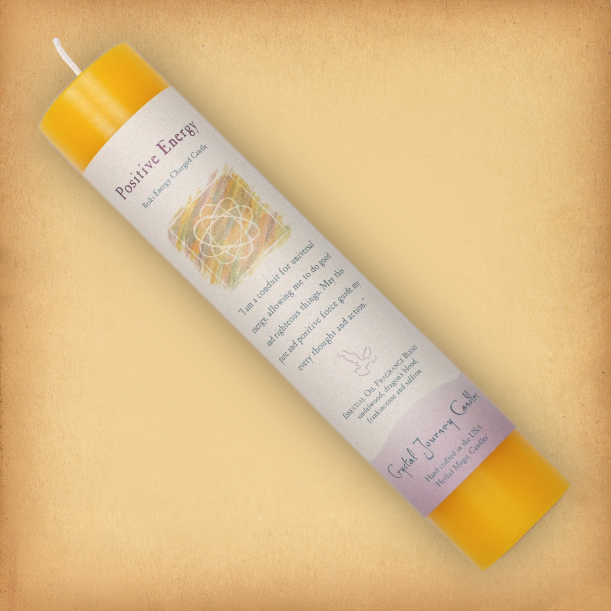 Yellow Reiki-charged Positive Energy Pillar Candle, laid diagonally to show label with affirmation and essential oil blend.