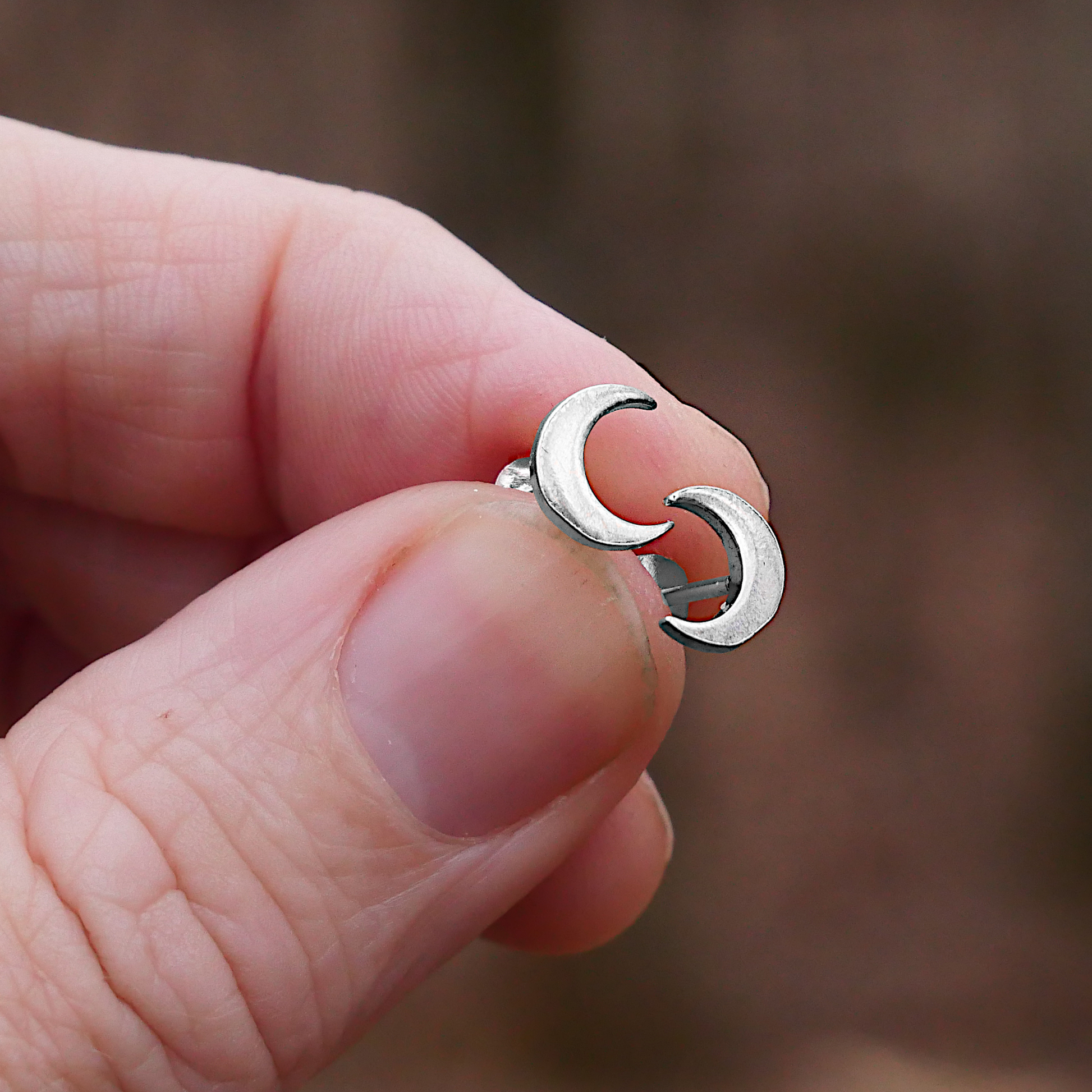 Closeup of Silver New Moon Post Earrings, sleek crescent silhouettes, held in a woman's fingertips.