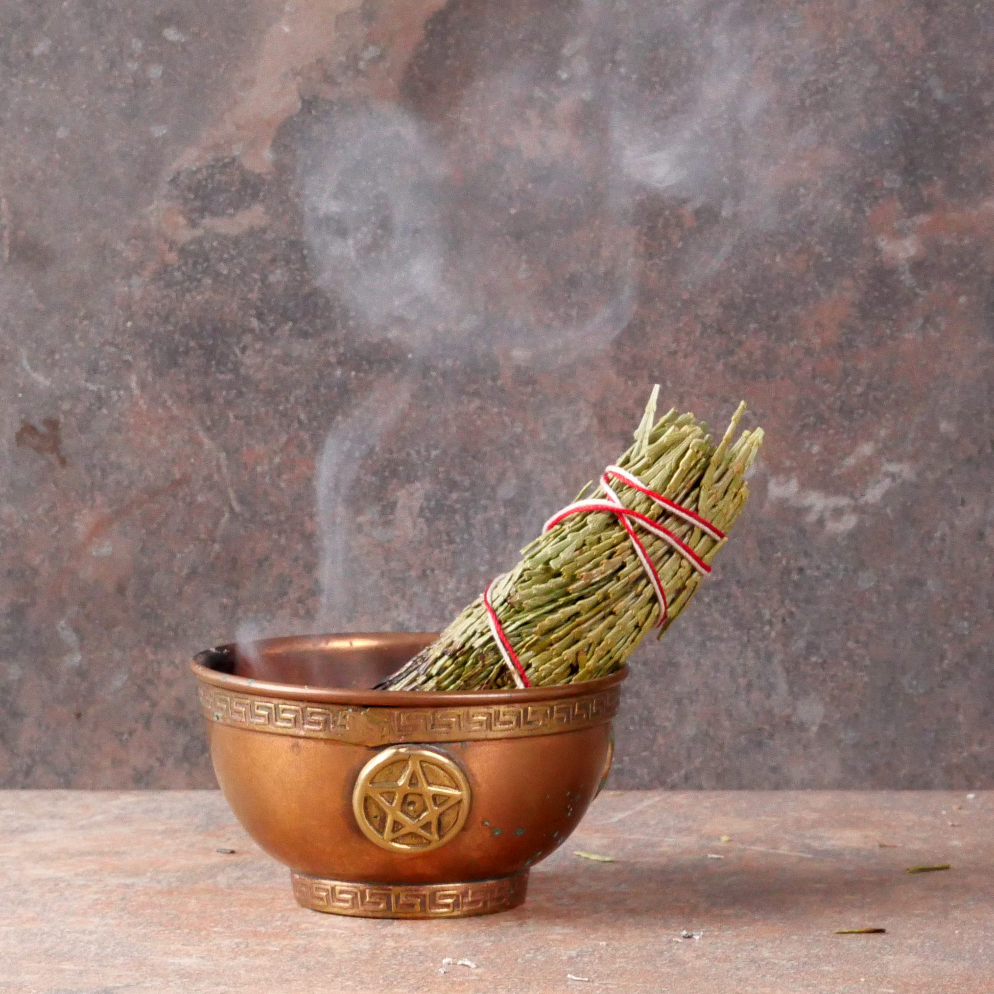 Smoldering Cedar Herb Bundle with a thin stream of smoke, propped in a small copper bowl that sits on fireproof tile surface