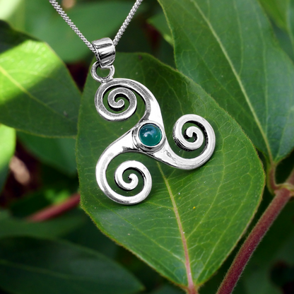 Sterling Silver Triskele Pendant with green agate stone, resting on vibrant green leaves, showcasing its Celtic-inspired design.
