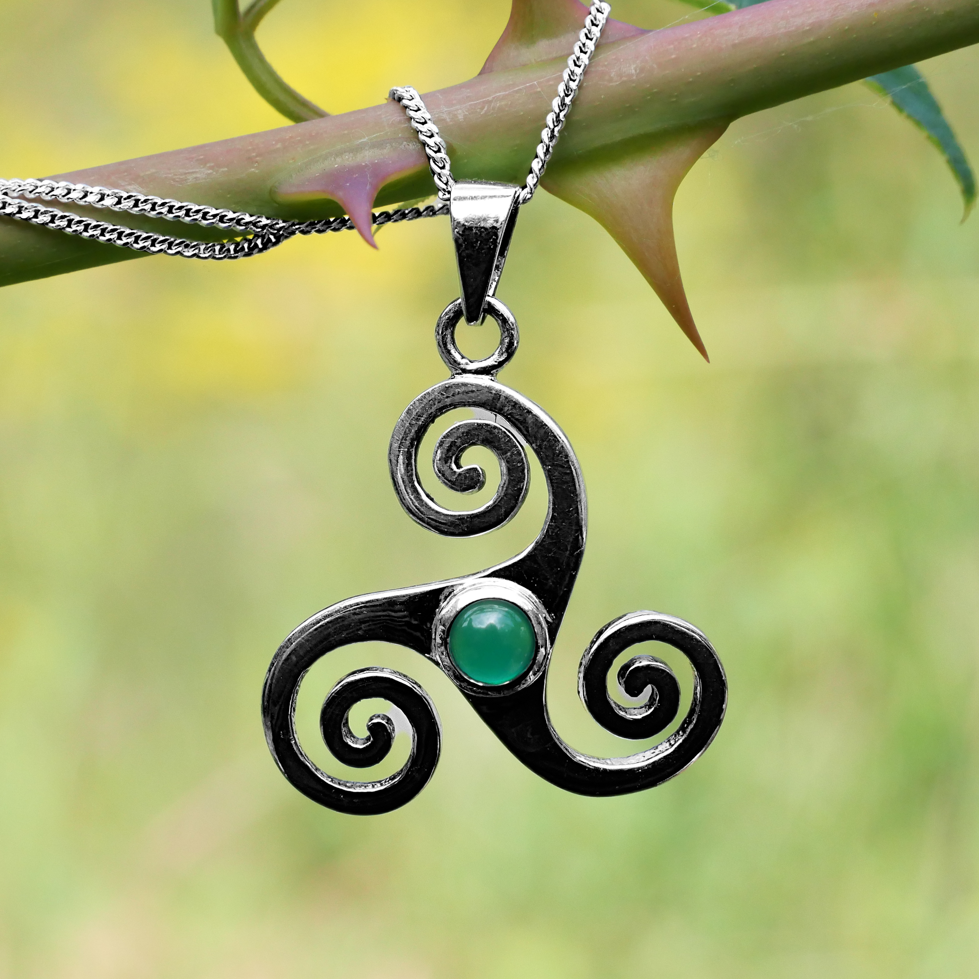 Sterling Silver Triskele Pendant with green agate, draped over a rose stem with thorns, highlighting its dramatic silhouette.
