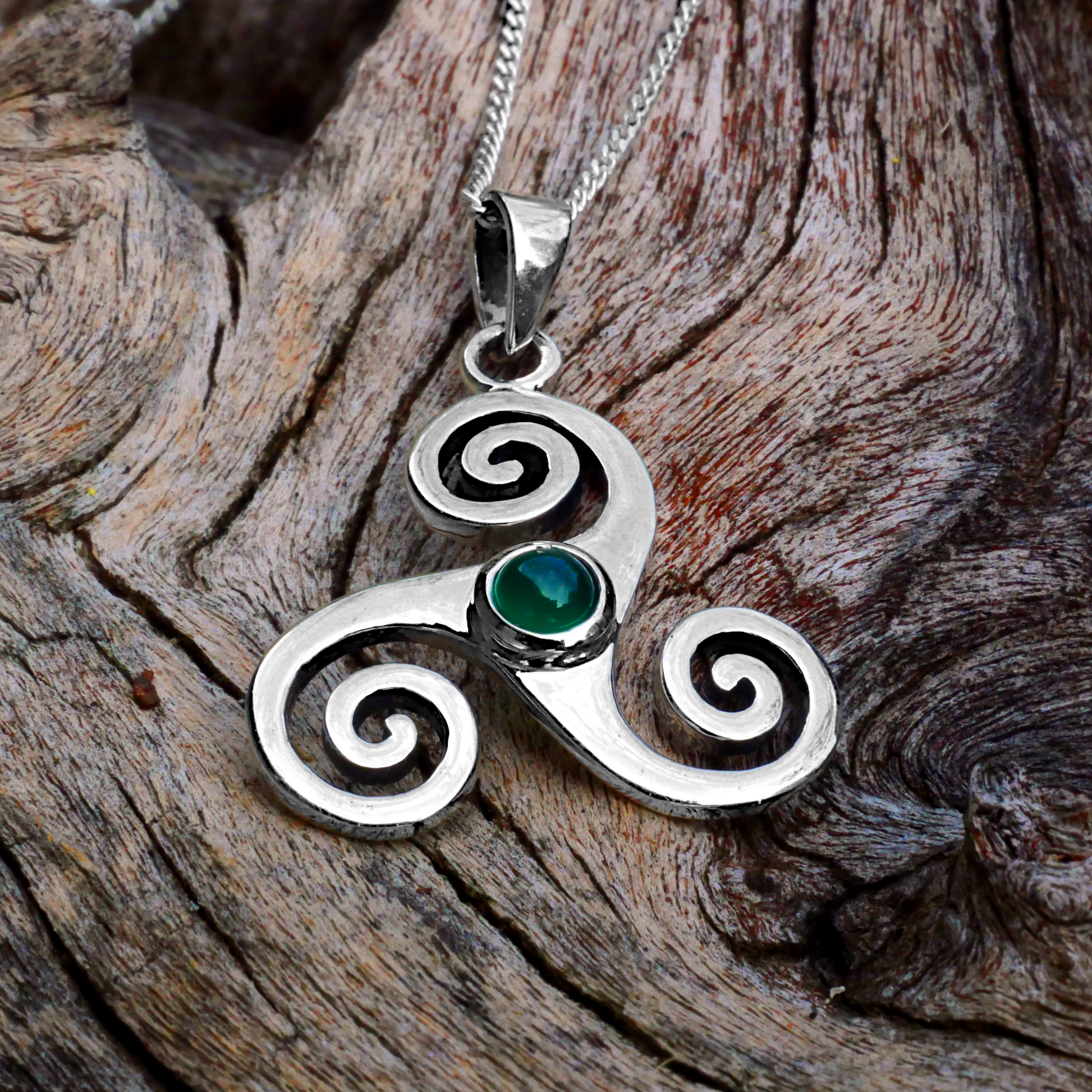 Sterling Silver Triskele Pendant with green agate stone, displayed on rough driftwood, highlighting its connection to Nature.
