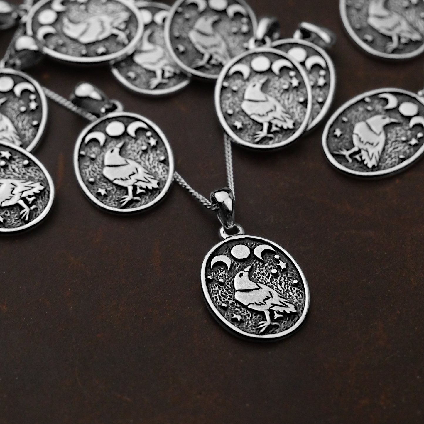 A collection of Silver Raven Moon Pendants displayed on a dark surface, showcasing its celestial and mystical design.