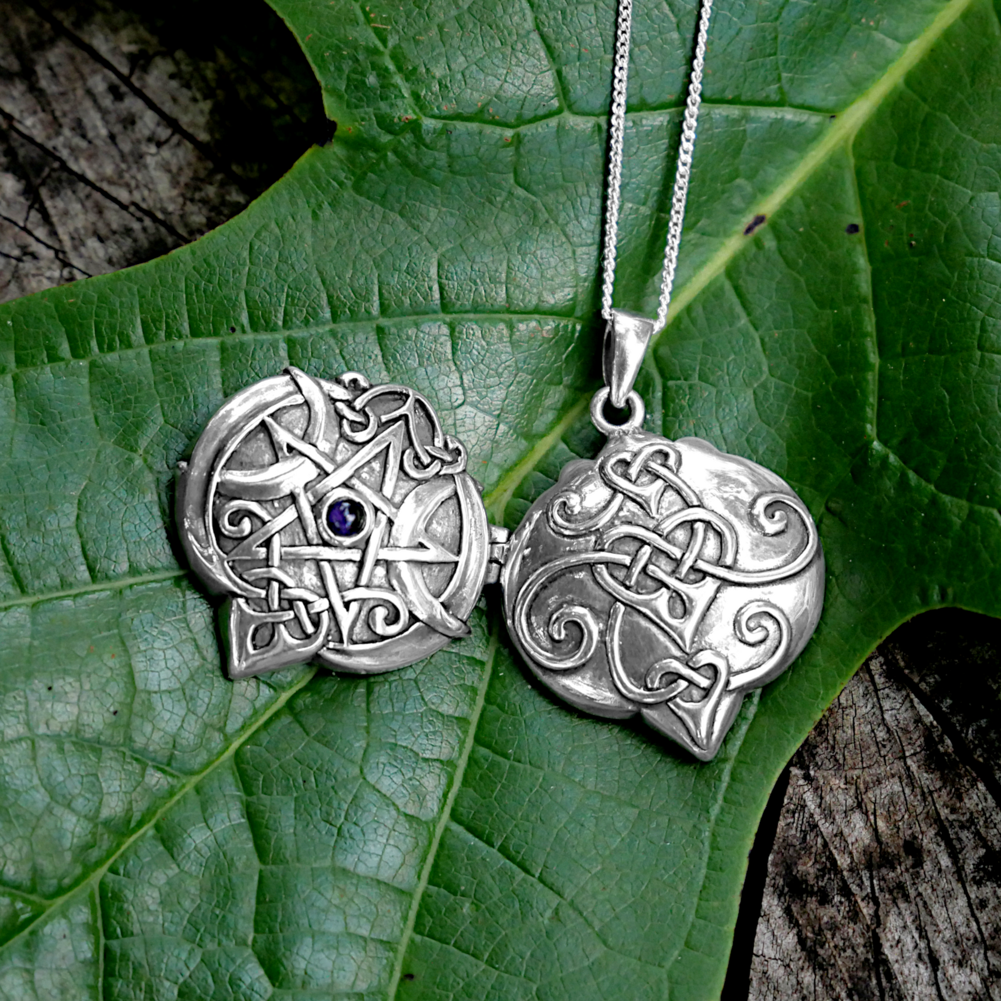Silver Amethyst Heart Pentacle Locket, displayed open to reveal its pagan and Celtic designs, photographed on a green leaf.