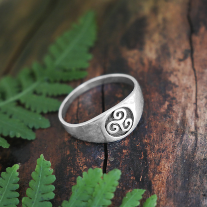 Silver Triskele Signet Ring with a Celtic-inspired triple spiral design, displayed on a fallen log framed by fern fronds.