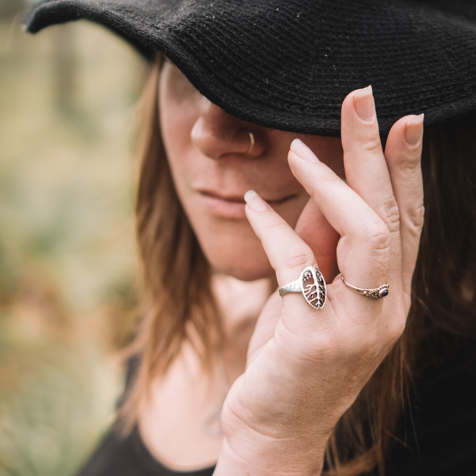 A woman tilts her hat while wearing a Silver Tree of Life Ring with an openwork design of branches and roots.