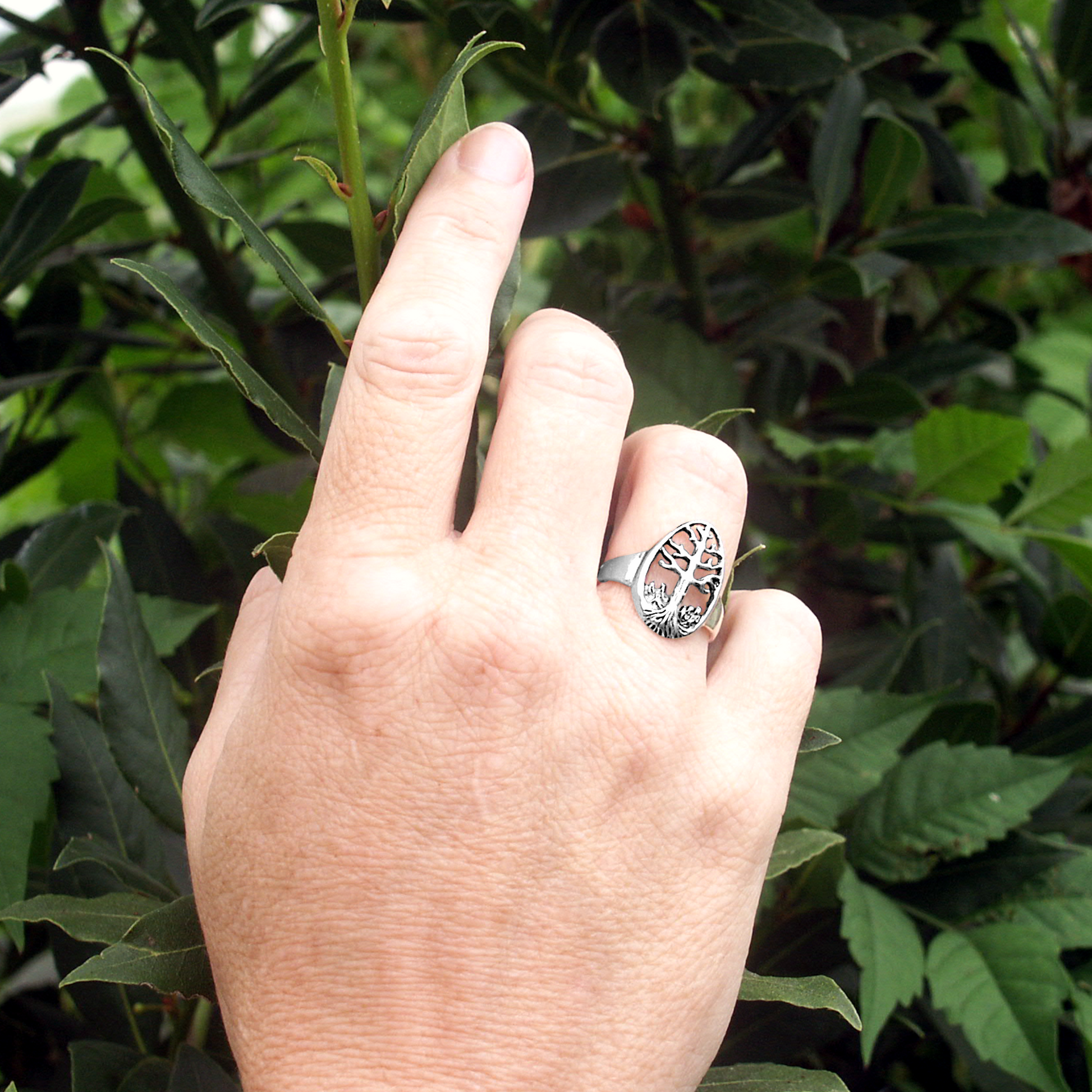 Silver Tree of Life Ring displayed on a hand, with green foliage in the background for an organic, nature-inspired setting.