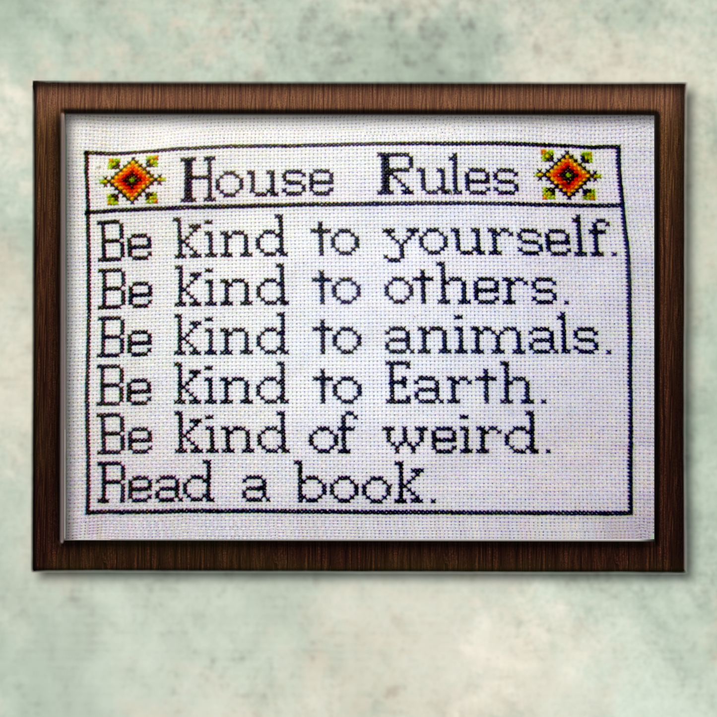 Framed House Rules cross stitch project, fully stitched and displayed on a wall, featuring list of kindness-themed reminders.