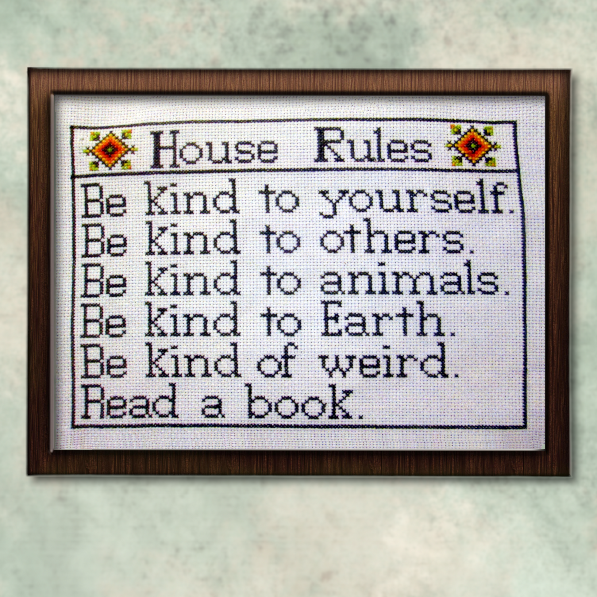 Framed House Rules cross stitch project, fully stitched and displayed on a wall, featuring list of kindness-themed reminders.