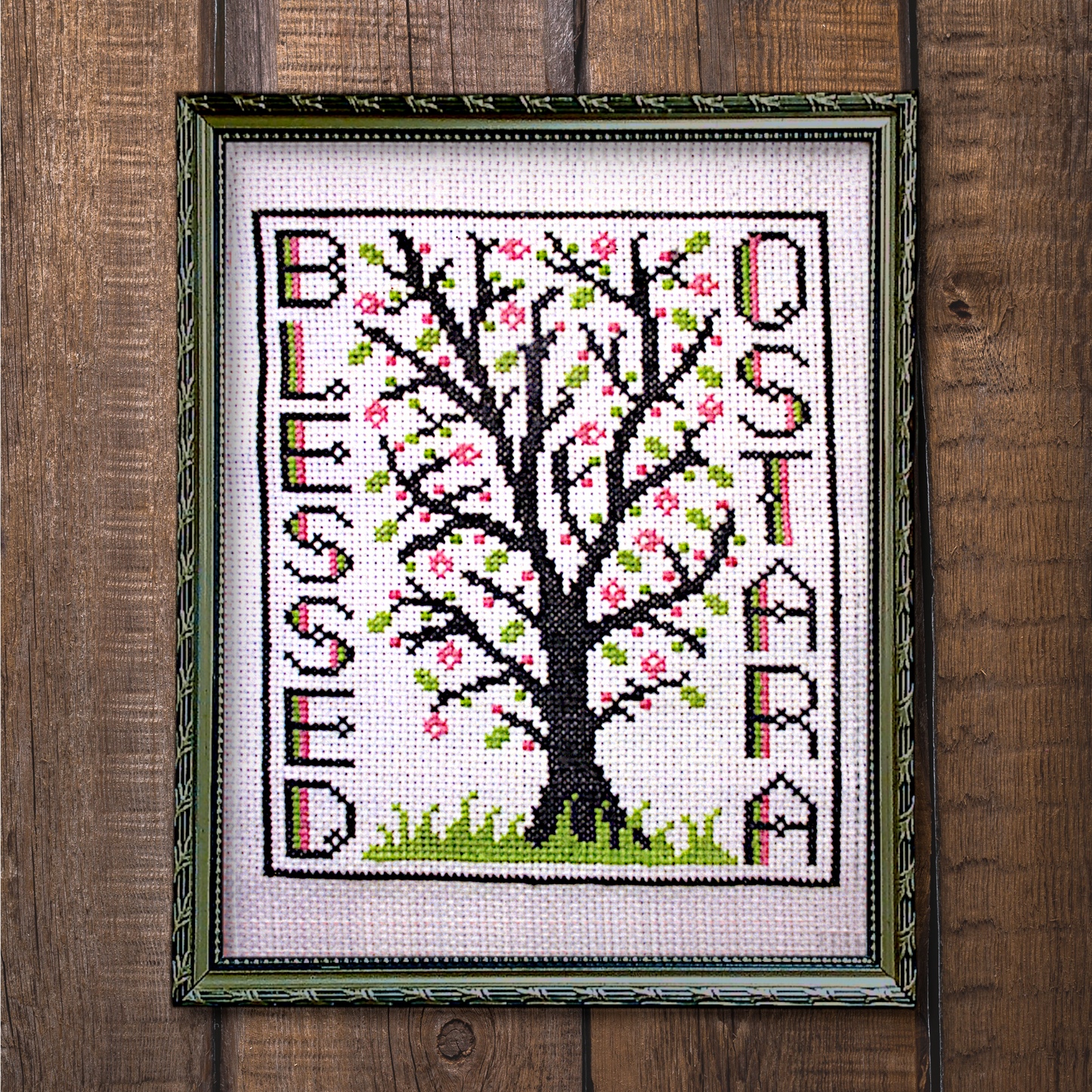 Framed Blessed Ostara cross stitch project, fully stitched and displayed on a wooden background, featuring a tree in bloom.