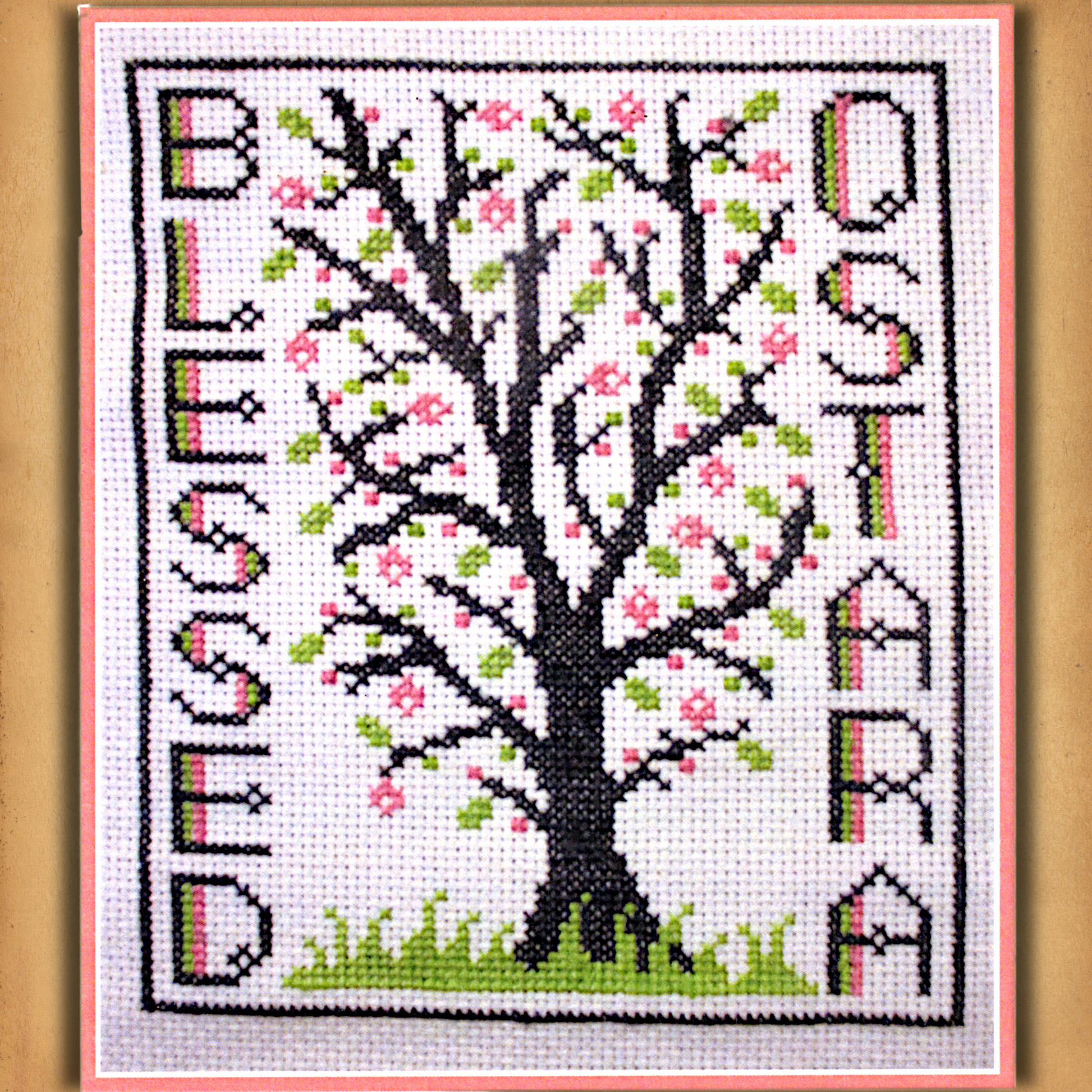 Blessed Ostara cross stitch design featuring a tree with pink blossoms and green leaves, framed by the words “Blessed Ostara”
