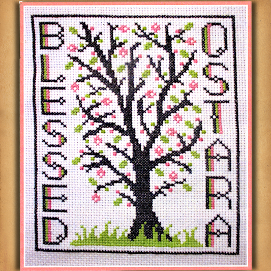 Blessed Ostara cross stitch design featuring a tree with pink blossoms and green leaves, framed by the words “Blessed Ostara”